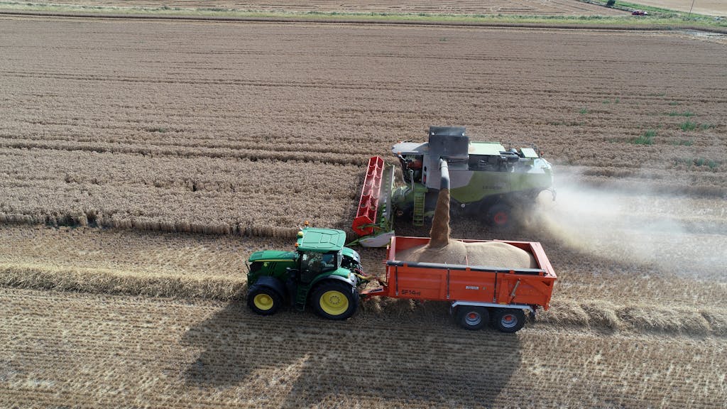 Green Machine Gathering Grain and Pouring It into Red and Green Tractor on the Field